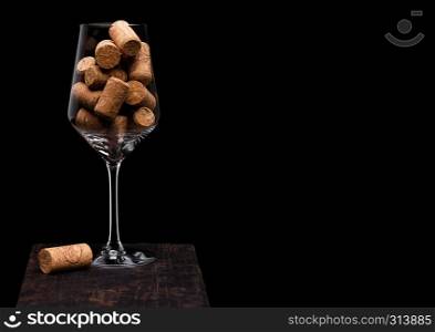 Wine glass with corks inside with cork next to glass on wooden board on black