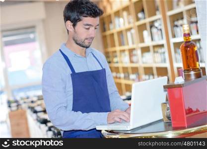 wine shop assistant checking info on his laptop