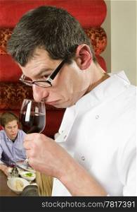 wine waiter savouring wine in a restaurant witch customers on the background