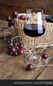 wineglass in front of grapes on a basket to serve wine with bottle on a rustic wooden background