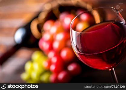 Wineglass with red wine on a background of grape and bottle on wooden table. Red wine close up