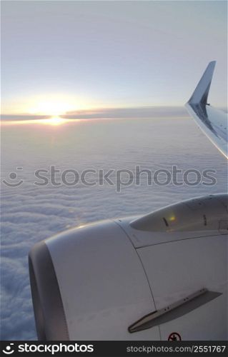 Wing and engine of an airplane flying above the clouds at sunset