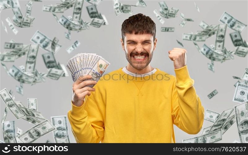 winning, finance and people concept - happy smiling young man in yellow sweatshirt with money celebrating success over grey background. happy young man with money celebrating success
