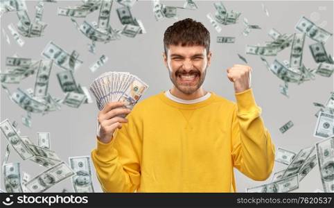 winning, finance and people concept - happy smiling young man in yellow sweatshirt with money celebrating success over grey background. happy young man with money celebrating success