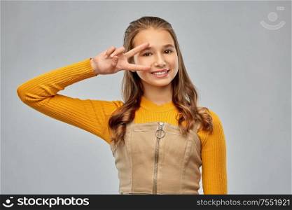 winning gesture, emotions and people concept - happy smiling young teenage girl showing peace hand sign over grey background. smiling young teenage girl showing peace hand sign