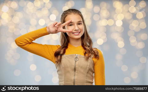 winning gesture, emotions and people concept - happy smiling young teenage girl showing peace hand sign over festive lights background. smiling young teenage girl showing peace hand sign