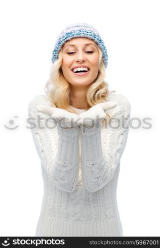 winter, advertisement, christmas and people concept - smiling young woman in winter hat and sweater holding something on her empty palms