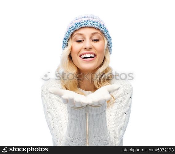 winter, advertisement, christmas and people concept - smiling young woman in winter hat and sweater holding something on her empty palms