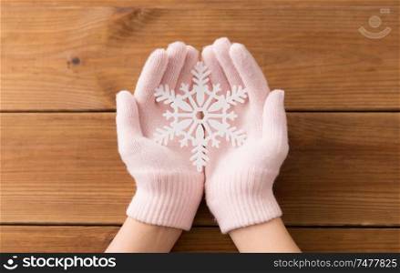 winter and christmas concept - hands in pale pink woollen gloves holding big white snowflake over wooden boards background. hands in pale pink gloves holding big snowflake