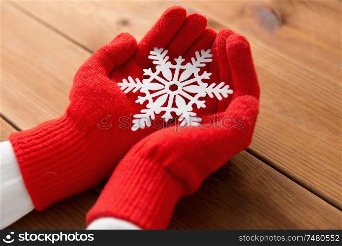 winter and christmas concept - hands in red woollen gloves holding big white snowflake over wooden boards background. hands in red woollen gloves holding big snowflake