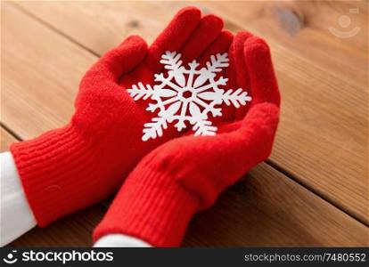 winter and christmas concept - hands in red woollen gloves holding big white snowflake over wooden boards background. hands in red woollen gloves holding big snowflake