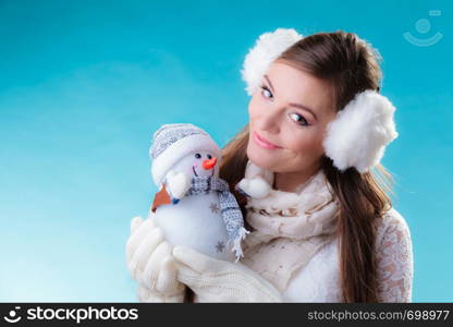 Winter and Christmas time concept. Woman teen girl in warm clothes holding happy nice snowman toy. Studio shot on blue background