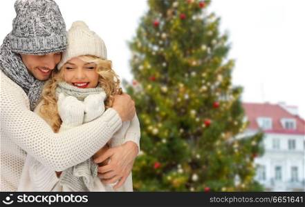 winter and holidays concept - happy couple in hats and scarves hugging over christmas tree at tallinn old town hall square background. happy couple hugging over christmas tree