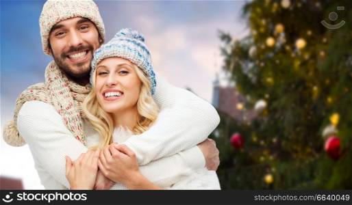 winter and holidays concept - happy couple in hats hugging over christmas tree at tallinn old town hall square background. happy couple hugging over christmas tree