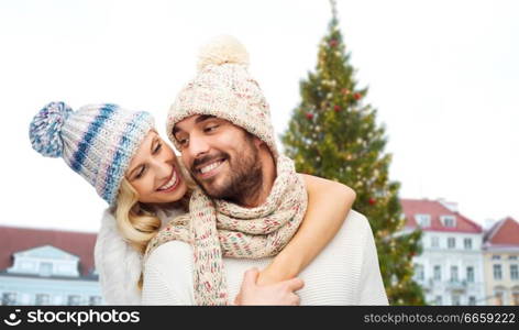 winter and holidays concept - happy couple in hats hugging over christmas tree at tallinn old town hall square background. happy couple hugging over christmas tree