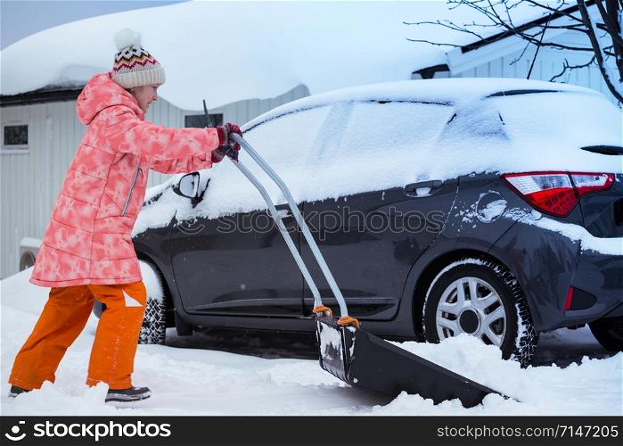 winter and snowfall. child girl cleans snow with a shovel