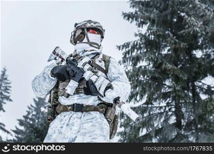 Winter arctic mountains warfare. Action in cold conditions. Trooper with weapons in forest somewhere above the Arctic Circle. Low angle view. Winter arctic warfare