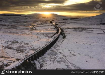 Winter Ariel picture of Yorkshire landmark Ribblehead Viaduct, North Yorkshire, The Ribblehead Viaduct or Batty Moss Viaduct carries the Settle?Carlisle railway across Batty Moss in the Ribble Valley at Ribblehead, in North Yorkshire, England. The viaduct, built by the Midland Railway, is 28 miles (45 km) north-west of Skipton and 26 miles (42 km) south-east of Kendal. It is a Grade II* listed structure.[1] Ribblehead Viaduct is the longest and the third tallest structure on the Settle?Carlisle line.The viaduct was designed by John Sydney Crossley, chief engineer of the Midland Railway, who was responsible for the design and construction of all major structures along the line. The viaduct was necessitated by the challenging terrain of the route. Construction began in late 1869. It necessitated a large workforce, up to 2,300 men, most of whom lived in shanty towns set up near its base. Over 100 men lost their lives during its construction. The Settle to Carlisle line was the last main railway in Britain to be constructed primarily with manual labour.