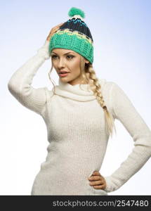 winter blond girl with tress hair and green hat white sweater looking on one side