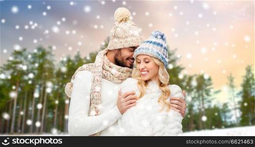 winter, christmas and people concept - happy couple in hats and scarf hugging over forest background. couple hugging over winter forest background
