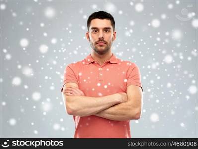 winter, christmas and people concept - serious young man in polo t-shirt with crossed arms over snow on gray background