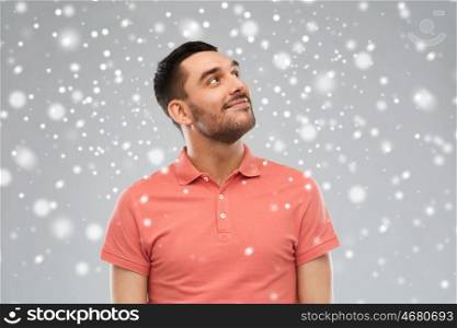 winter, christmas, idea, inspiration and people concept - happy smiling young man in polo t-shirt looking up over snow on gray background