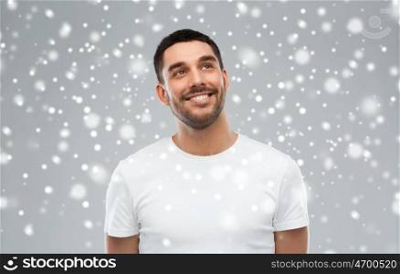 winter, christmas, idea, inspiration and people concept - happy smiling young man looking up over snow on gray background