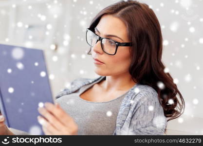winter, christmas, literature, education and people concept - young woman in glasses reading book at home