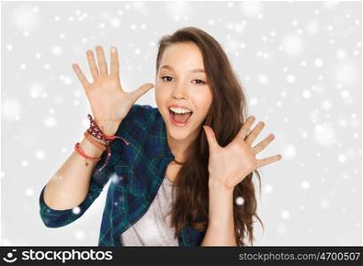 winter, christmas, people and teens concept - happy laughing pretty teenage girl showing hands over gray background and snow