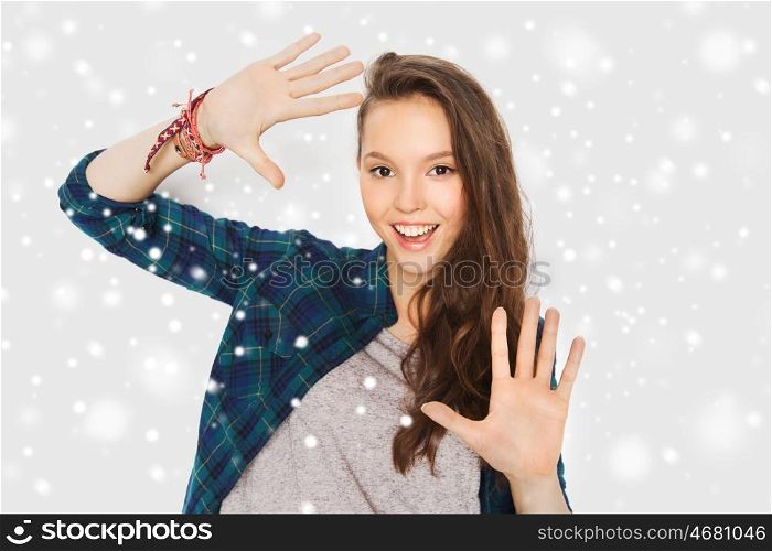 winter, christmas, people and teens concept - happy smiling pretty teenage girl showing hands over gray background and snow