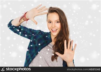 winter, christmas, people and teens concept - happy smiling pretty teenage girl showing hands over gray background and snow