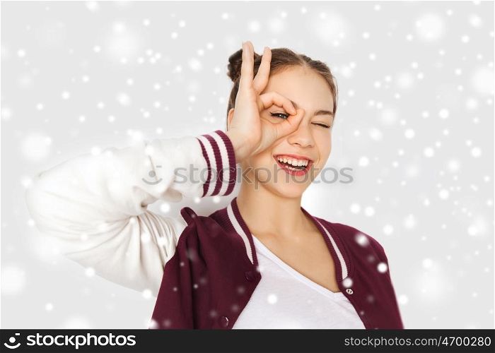 winter, christmas, people and teens concept - happy smiling pretty teenage girl making face and having fun over gray background and snow