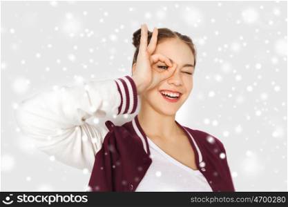 winter, christmas, people and teens concept - happy smiling pretty teenage girl making face and having fun over gray background and snow