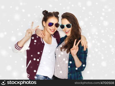 winter, christmas, people, fashion and gesture concept - happy smiling pretty teenage girls or friends in sunglasses showing peace hand sign over gray background and snow