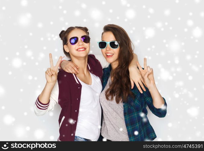winter, christmas, people, fashion and gesture concept - happy smiling pretty teenage girls or friends in sunglasses showing peace hand sign over gray background and snow