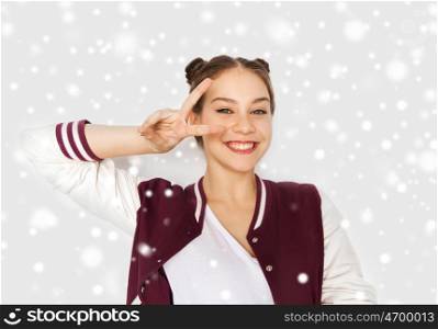 winter, christmas, people, gesture and teens concept - happy smiling pretty teenage girl showing peace sign over gray background and snow