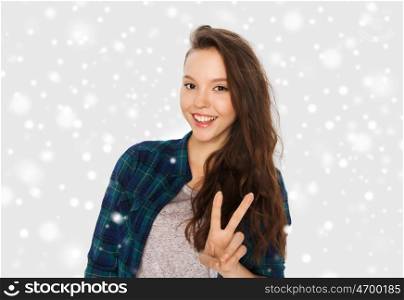 winter, christmas, people, gesture and teens concept - happy smiling pretty teenage girl showing peace sign over gray background and snow