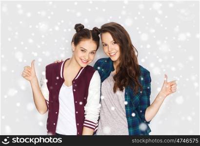 winter, christmas, people, gesture and teens concept - happy smiling pretty teenage girls hugging and showing thumbs up over gray background and snow