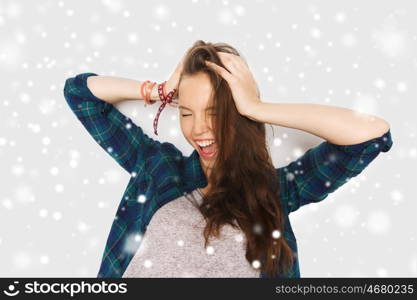 winter, christmas, people, hair care, style and teens concept - happy pretty teenage girl holding to head over gray background and snow