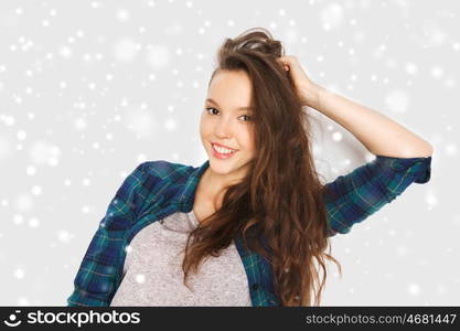 winter, christmas, people, hair care, style and teens concept - happy smiling pretty teenage girl touching her head over gray background and snow