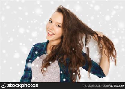 winter, christmas, people, hair care, style and teens concept - happy smiling pretty teenage girl touching her head over gray background and snow. happy smiling pretty teenage girl
