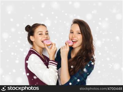 winter, christmas, people, holidays and fast food concept - happy smiling pretty teenage girls or friends with donuts eating and having fun over gray background and snow
