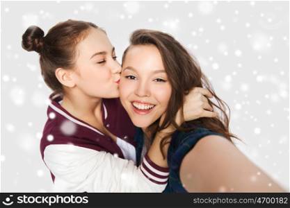 winter, christmas, people, teens and friendship concept - happy smiling pretty teenage girls or friends taking selfie and kissing over gray background and snow
