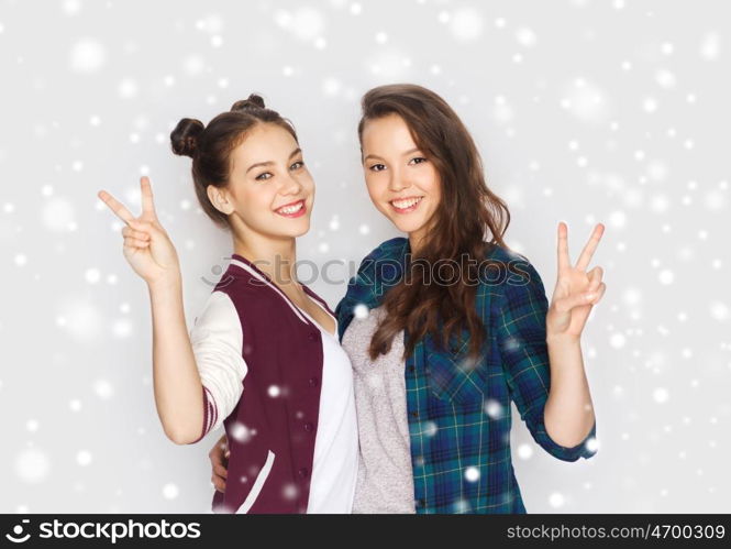 winter, christmas, people, teens and friendship concept - happy smiling pretty teenage girls or friends hugging and showing peace hand sign over gray background and snow