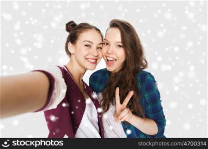 winter, christmas, people, teens and friendship concept - happy smiling pretty teenage girls or friends taking selfie and showing peace sign over gray background and snow