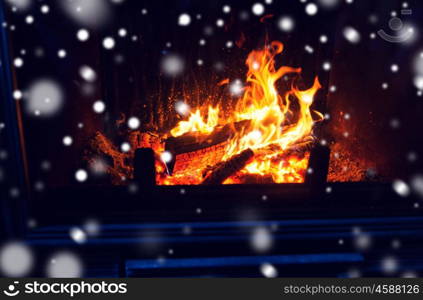 winter, christmas, warmth, fire and coziness concept - close up of burning fireplace with snow