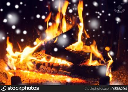 winter, christmas, warmth, fire and coziness concept - close up of firewood burning in fireplace with snow