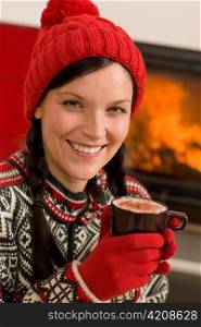 Winter Christmas woman with hat and gloves drink by fireplace