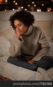 winter, comfort and people concept - sad woman in woolen sweater sitting on bed at home at night. sad woman in sweater on bed at home at night