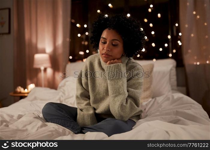 winter, comfort and people concept - sad woman in woolen sweater sitting on bed at home at night. sad woman in sweater on bed at home at night